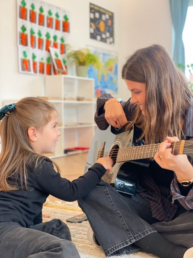 Ms.Erletë playing the guitar next to a child